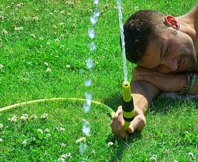 muž leží na trávě a drží hadici s vodou
